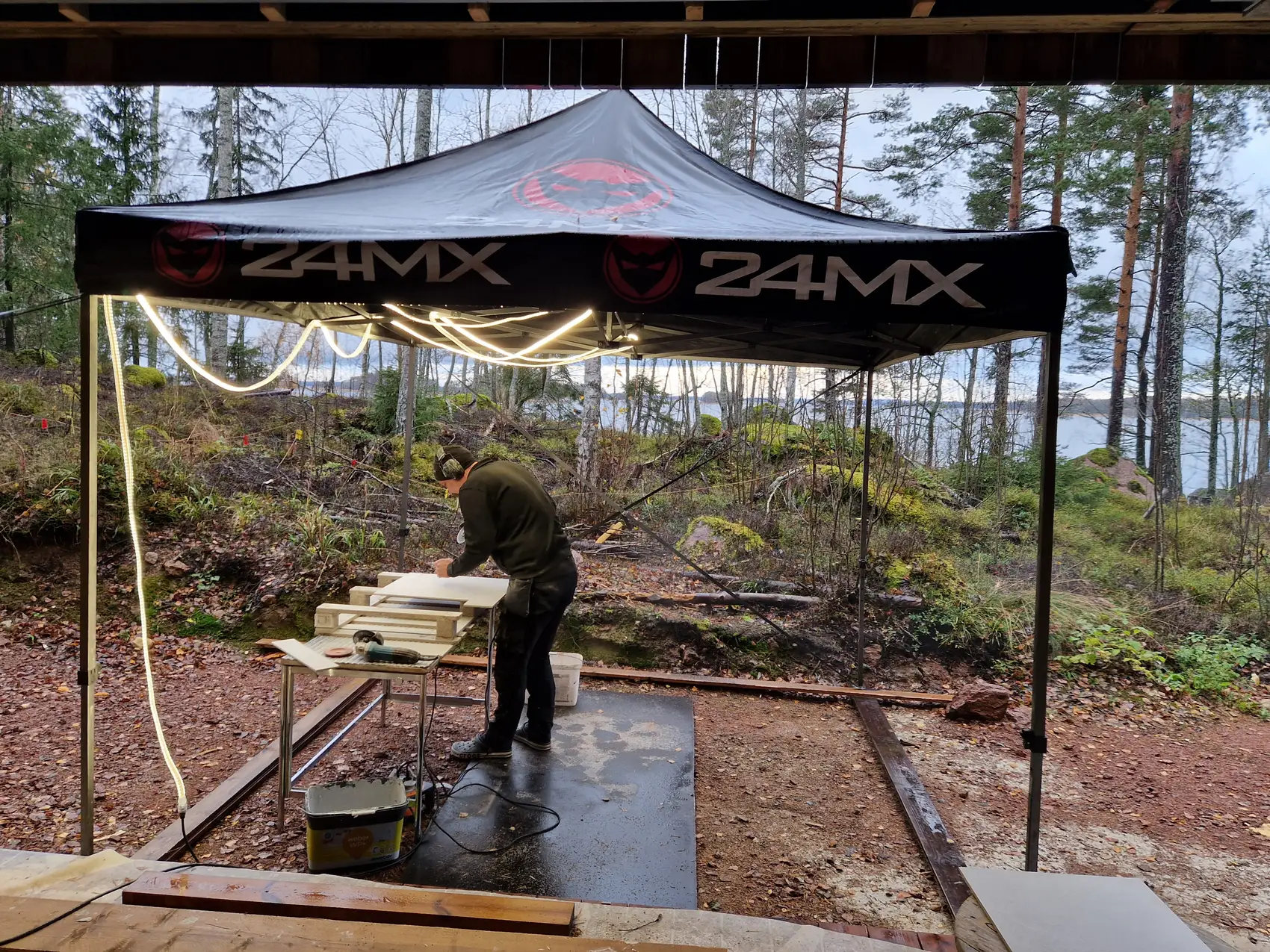 Lajaxin laatoittaja leikkaa laattoja teltan alla järvenrantatyömaalla
