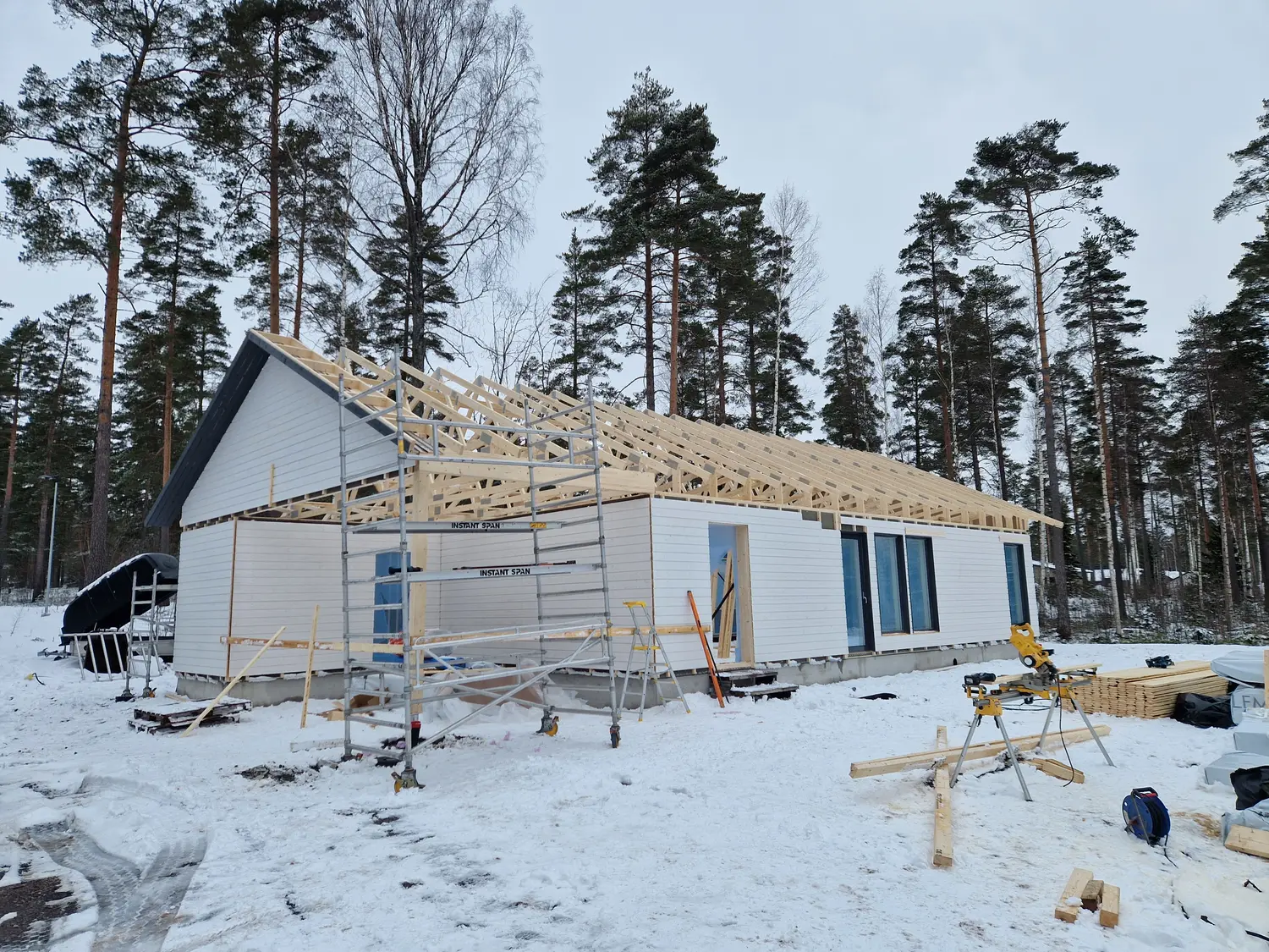 Omakotitalo rakenteilla talvella, kattoristikot paikoillaan ja telineet seinän vieressä